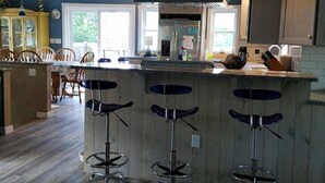 A kitchen with wooden cabinets, a central island with stools, a ceiling fan, and a view to the outside. - Beautifully Renovated, Central AC, wash/dryer, dishwasher, New Appliances. (Charlestown)
