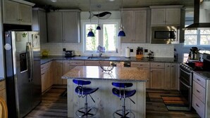 A modern kitchen with wooden cabinets, a stainless steel refrigerator, a microwave, and a large island with bar stools. - Beautifully Renovated, Central AC, wash/dryer, dishwasher, New Appliances. (Charlestown)