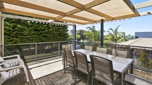 An outdoor patio with a table and chairs, a wooden deck, and a view of trees and buildings. - Torquay Sea-Cret (Torquay)