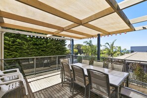 Eine Terrasse im Freien mit Tisch und Stühlen, ein Holzdeck und Blick auf Bäume und Gebäude.