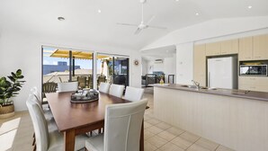 A modern kitchen with a central island, dining area with a large table and chairs, and a view through the glass doors. - Torquay Sea-Cret (Torquay)
