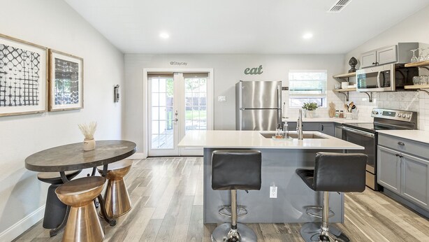 A modern kitchen with a central island, stainless steel appliances, and a dining area with stools. - Comfortable #Staycay Close to Everything In Dallas (Dallas)