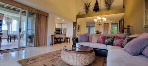 Ampla sala de estar com um sofá grande, uma mesa de centro redonda e um espaço de jantar com cadeiras e uma mesa.