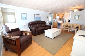 A living room with a brown leather sofa, a white coffee table, and a dining area with wooden chairs.