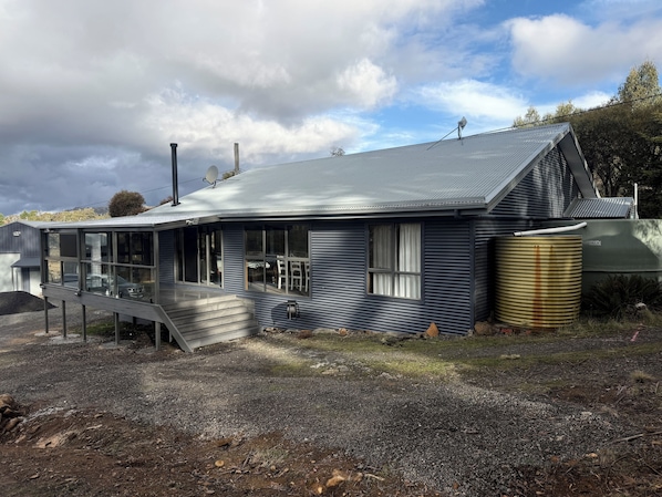 A single-story house with a covered porch, a satellite dish, and a large water tank. - Haddens Haven in Meena, Tasmania (Miena)