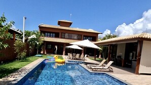 Una piscina con sillas de descanso y sombrillas, rodeada por un edificio con techo de tejas.