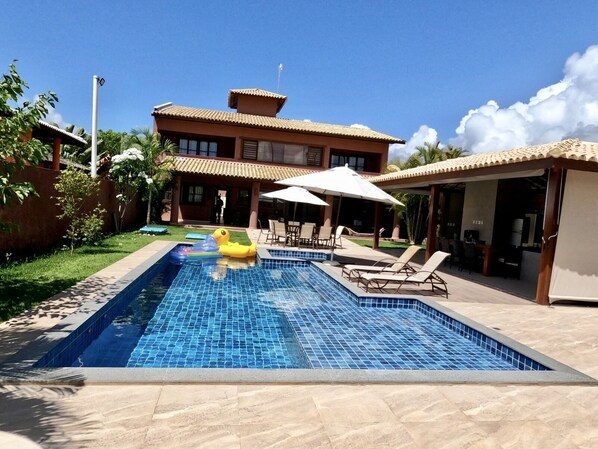 A swimming pool with lounge chairs and umbrellas, surrounded by a building with a tiled roof.
