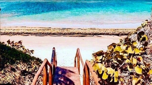 Una escalera de madera que da a una playa con aguas turquesas cristalinas.