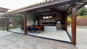 Un patio al aire libre con una mesa y sillas de madera, una zona de cocina con una isla grande y un espacio cubierto para sentarse.