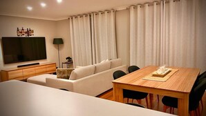Een moderne woonkamer met een flatscreen televisie, een bank, een eettafel en een lamp.