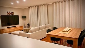 A modern living room with a flat-screen TV, a sofa, a dining table, and a lamp. - Villa Premiere - Cypress Lakes Resort (Pokolbin)