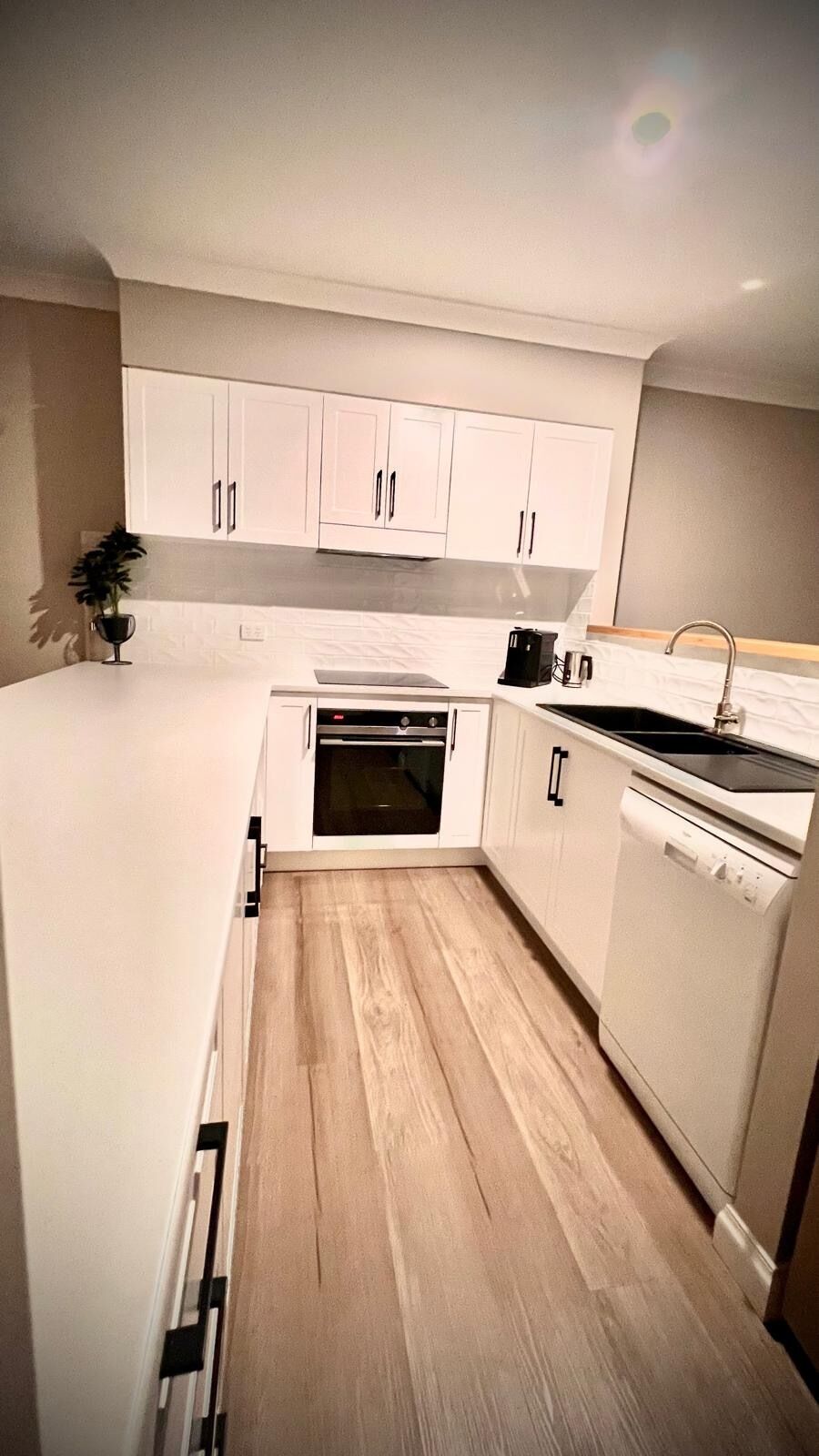 A modern kitchen with white cabinets, a built-in oven, and a dishwasher.