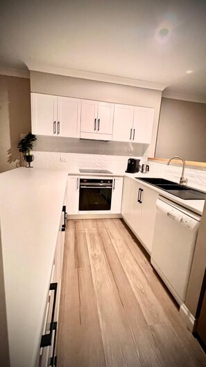 Une cuisine moderne avec des meubles blancs, un four encastré et un lave-vaisselle.