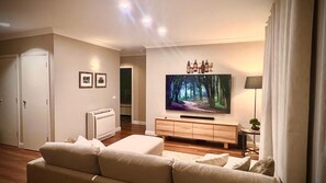 Een woonkamer met een flatscreen televisie, een bank, een kast en een deur naar een andere kamer.