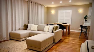 A living room with a sectional sofa, a dining table with chairs, and a small kitchen area.