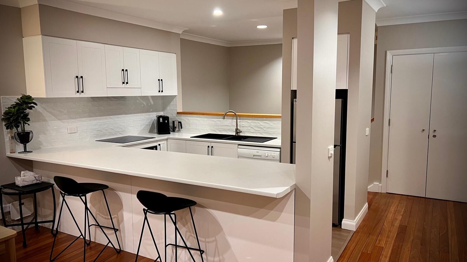 Une cuisine moderne avec des meubles blancs, un îlot central doté de tabourets, un évier et un réfrigérateur.