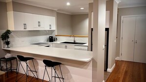 Een moderne keuken met witte kasten, een centraal eiland met krukken, een spoelbak en een koelkast.