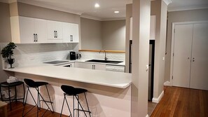A modern kitchen with white cabinets, a central island with stools, a sink, and a refrigerator. - Villa Premiere - Cypress Lakes Resort (Pokolbin)