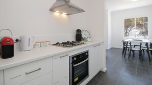 A modern kitchen with a gas stove, oven, and coffee maker. There is a dining area with a table and chairs.