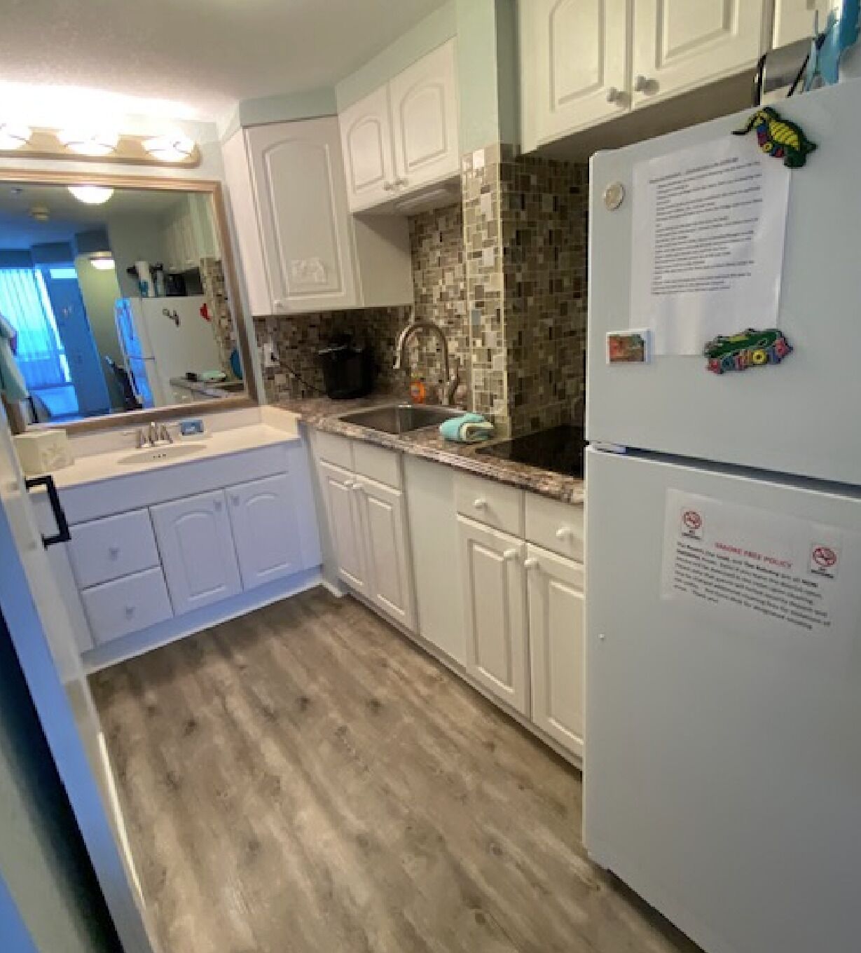 A kitchen with white cabinets, a tiled backsplash, and a wooden floor.