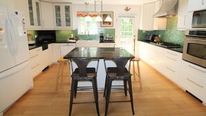 Una cocina moderna con armarios blancos, una isla central con taburetes, microondas, horno y cafetera.