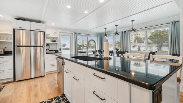 Una cocina moderna con un refrigerador de acero inoxidable, muebles blancos, una isla de vidrio con un lavamanos y ventanas amplias que ofrecen vistas de la ciudad.