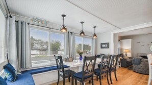 Una sala de estar moderna con comedor, ventanas grandes con cortinas y vistas al exterior.
