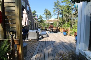 Una terraza de madera con mobiliario exterior, incluyendo sillas y una mesa, y una sombrilla grande que proporciona sombra.