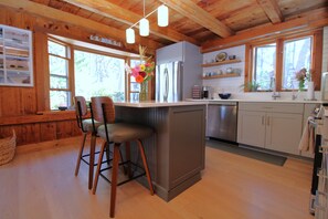 A kitchen with wooden beams, a central island with bar stools, a refrigerator, and a sink. - Lovely Post & Beam Near Indian Neck (1224) (Wellfleet)
