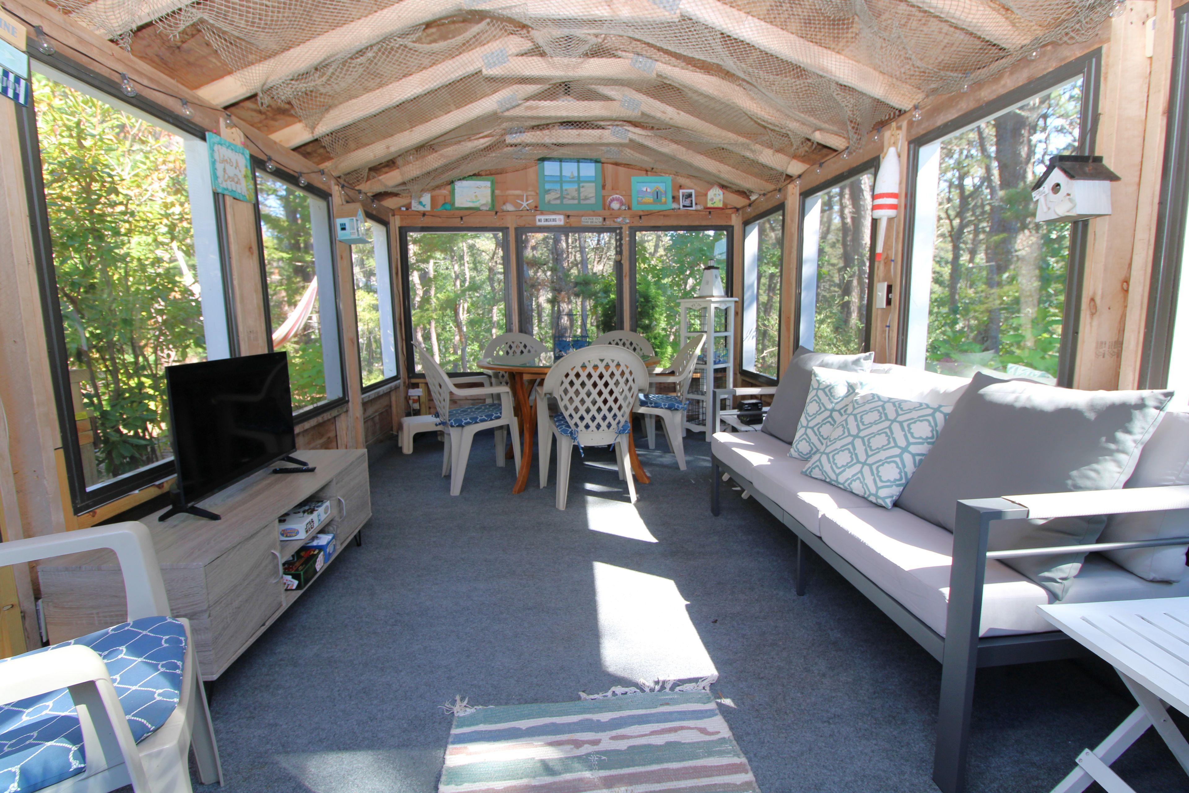 A covered outdoor seating area with a television, chairs, a sofa, and a table.