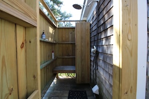 Un espace de douche extérieur en bois, avec un banc et une étagère.