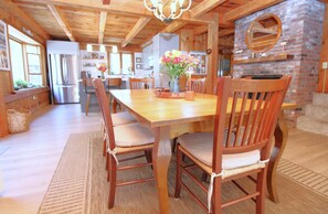 Una mesa de comedor de madera con sillas, una cocina al fondo y una chimenea de ladrillo.
