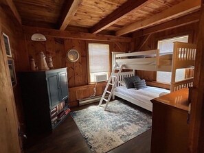 Una habitación tipo cabaña de madera con literas, un escritorio pequeño y una estantería.