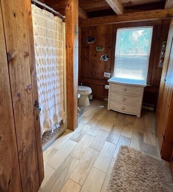 Un baño de cabaña de madera con un inodoro, un armario de madera y una ventana con persianas.