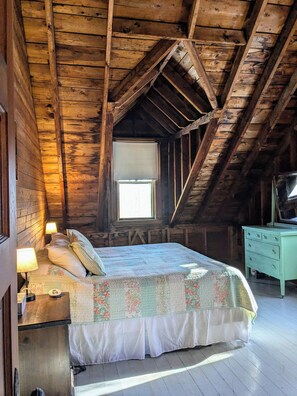 Cozy attic bedroom with a single bed, television, and small table.