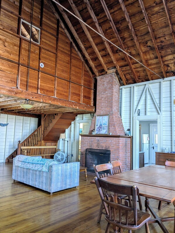 Cozy living space with a brick fireplace, dining area, and seating area, featuring a staircase and wooden paneling.