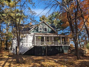 Surrounded by a dense forest, this cabin features a front porch and a small staircase leading to the entrance.