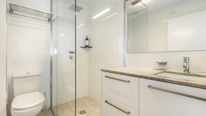 Un baño moderno con cabina de ducha de vidrio, inodoro, lavabo con espejo y encimera.