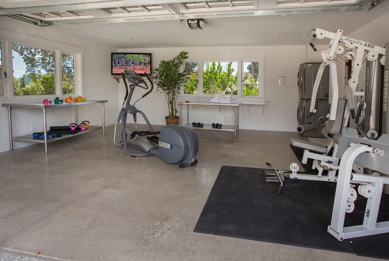 Une salle de sport à domicile équipée de matériel d’exercice, d’un tapis de course, de poids et d’un téléviseur fixé au mur.