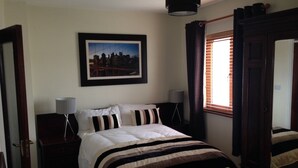 A bedroom with a bed, a nightstand, a lamp, a framed picture on the wall, and a window with curtains. - Cahirciveen Marina, Ring Of Kerry, 2bed/2bath House (Cahersiveen)