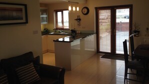 A modern kitchen with a central island, a dining area with a table and chairs, and a living room with a sofa. - Cahirciveen Marina, Ring Of Kerry, 2bed/2bath House (Cahersiveen)