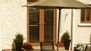 An outdoor patio with a glass table and chairs, a large umbrella, and potted plants. - Cahirciveen Marina, Ring Of Kerry, 2bed/2bath House (Cahersiveen)