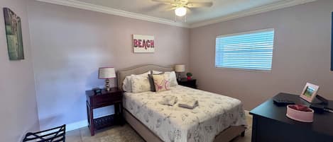 A bedroom with a bed, nightstands, a desk, a chair, a ceiling fan, a window with blinds, and a wall-mounted picture.