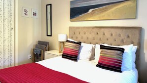 Een hotelkamer met een bed, een nachtkastje, een lamp en een schilderij van een strand.