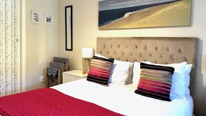 A hotel room with a bed, a nightstand, a lamp, and a painting of a beach scene. - Riversong City Retreat - right on the edge of town (Nelson City)