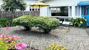 Een tuin met een kleine struik, een grindpad en een gele parasol.