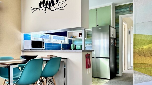 Een moderne keuken met smaragdgroene stoelen, een roestvrijstalen koelkast en een blauwe betegelde achterwand.