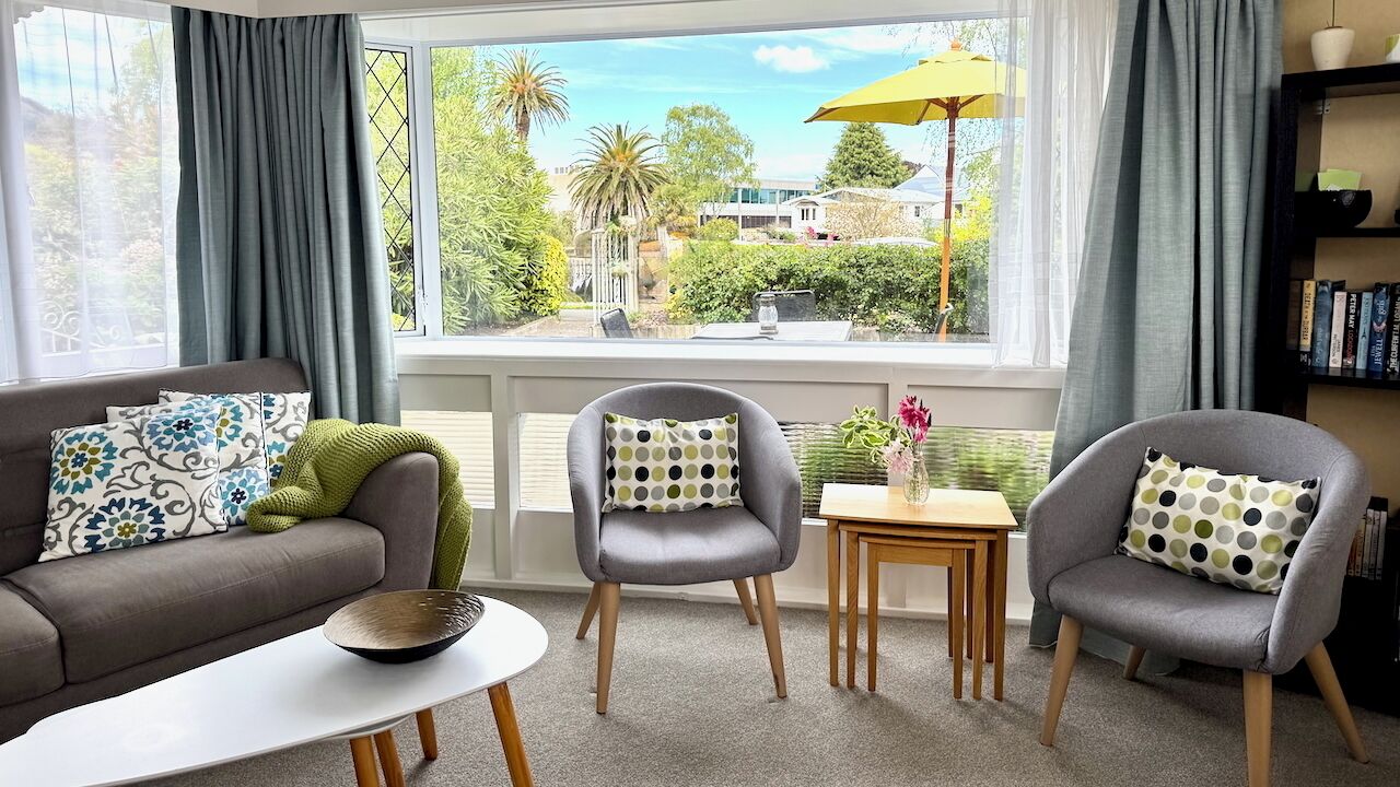 A living room with a sofa, two armchairs, a small table, and a view of greenery outside.