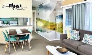 A modern living room with a sofa and chairs, a dining area with a table and chairs, and a kitchen area with appliances.