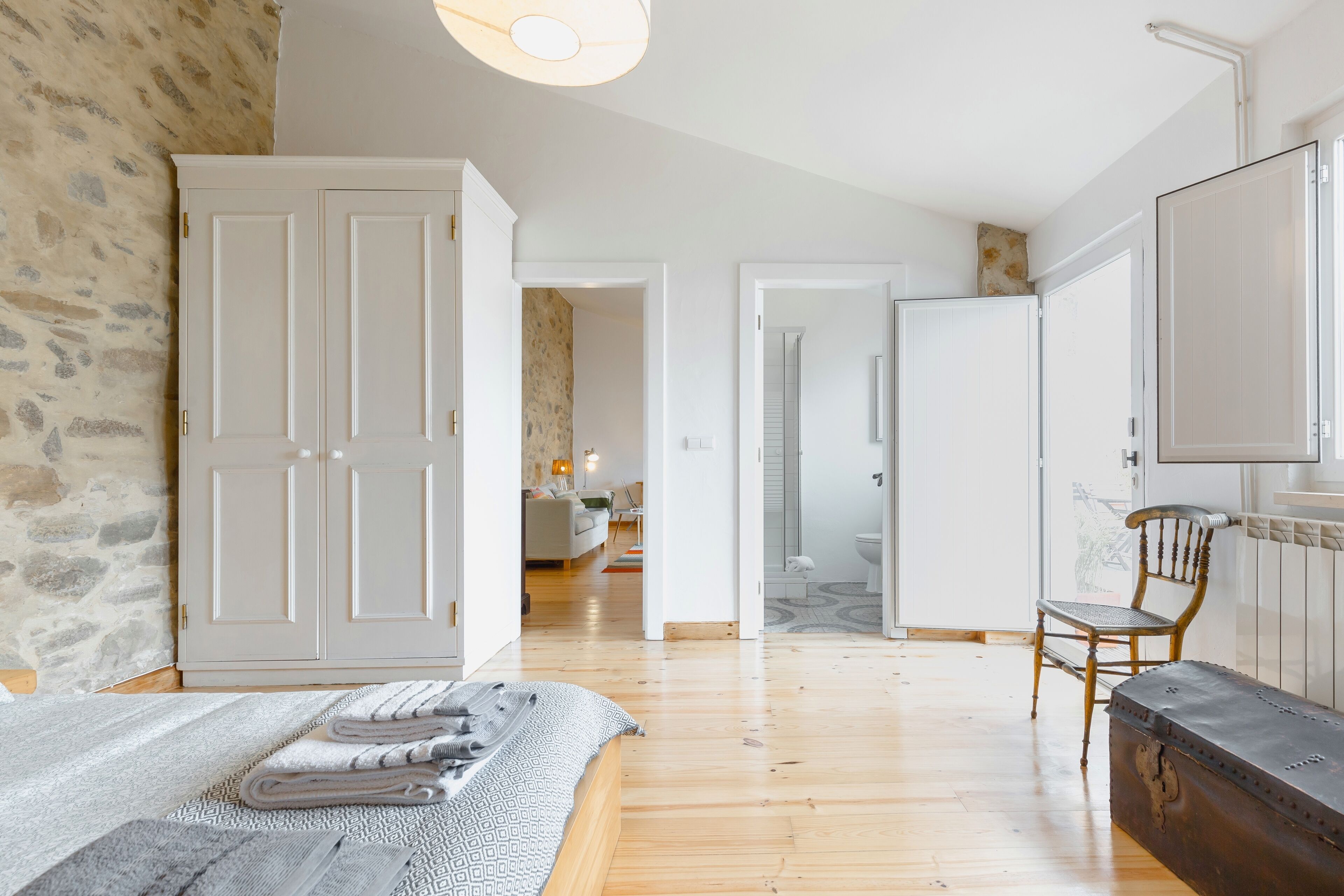 A spacious bedroom with a large bed, a wooden floor, a stone wall, and a wardrobe.